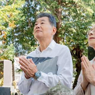 墓石に向かって手を合わせる老夫婦の姿